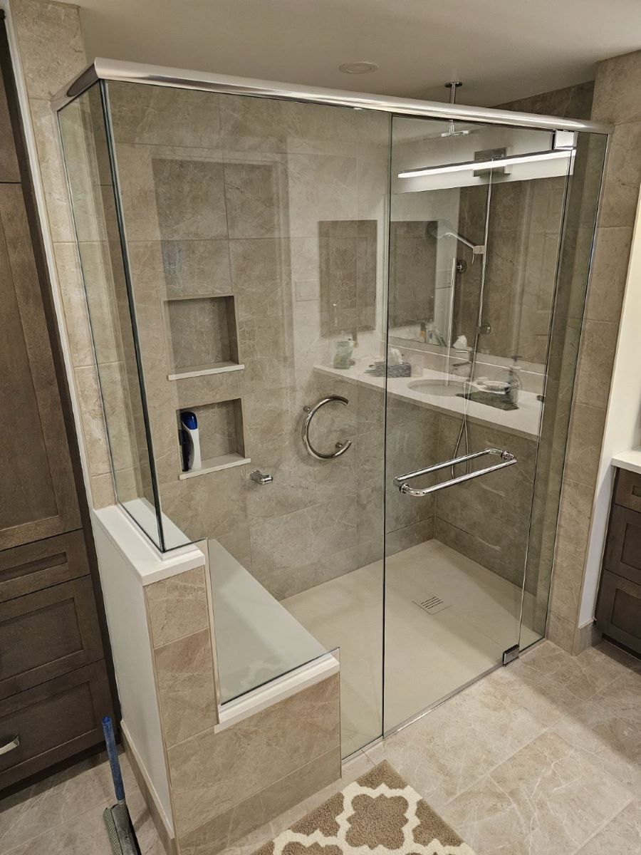 custom glass shower with a side panel and double notched piece of glass for the bench on the left side. pivot and header chrome hardware and double towel bar handle 