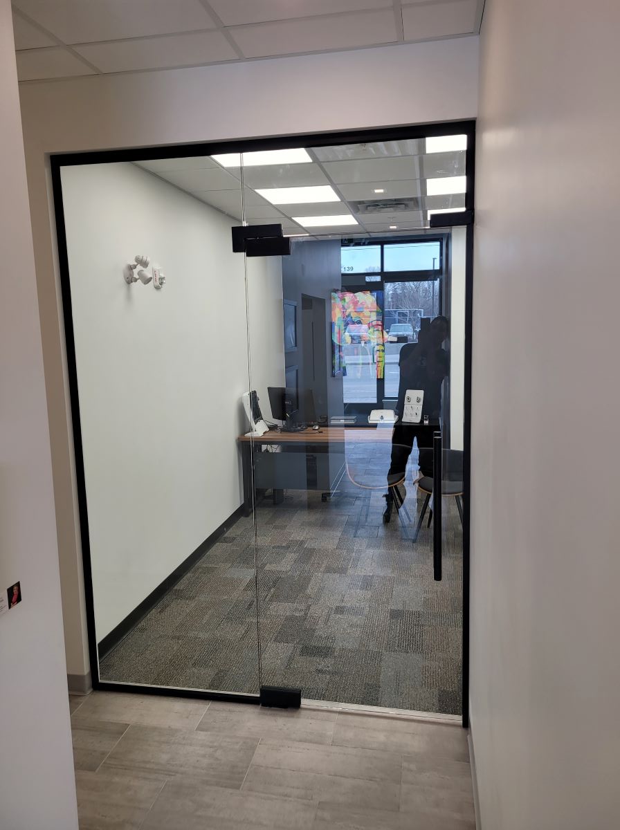 glass office with one hydraulic self closing door and a transom above the door with matte black hardware