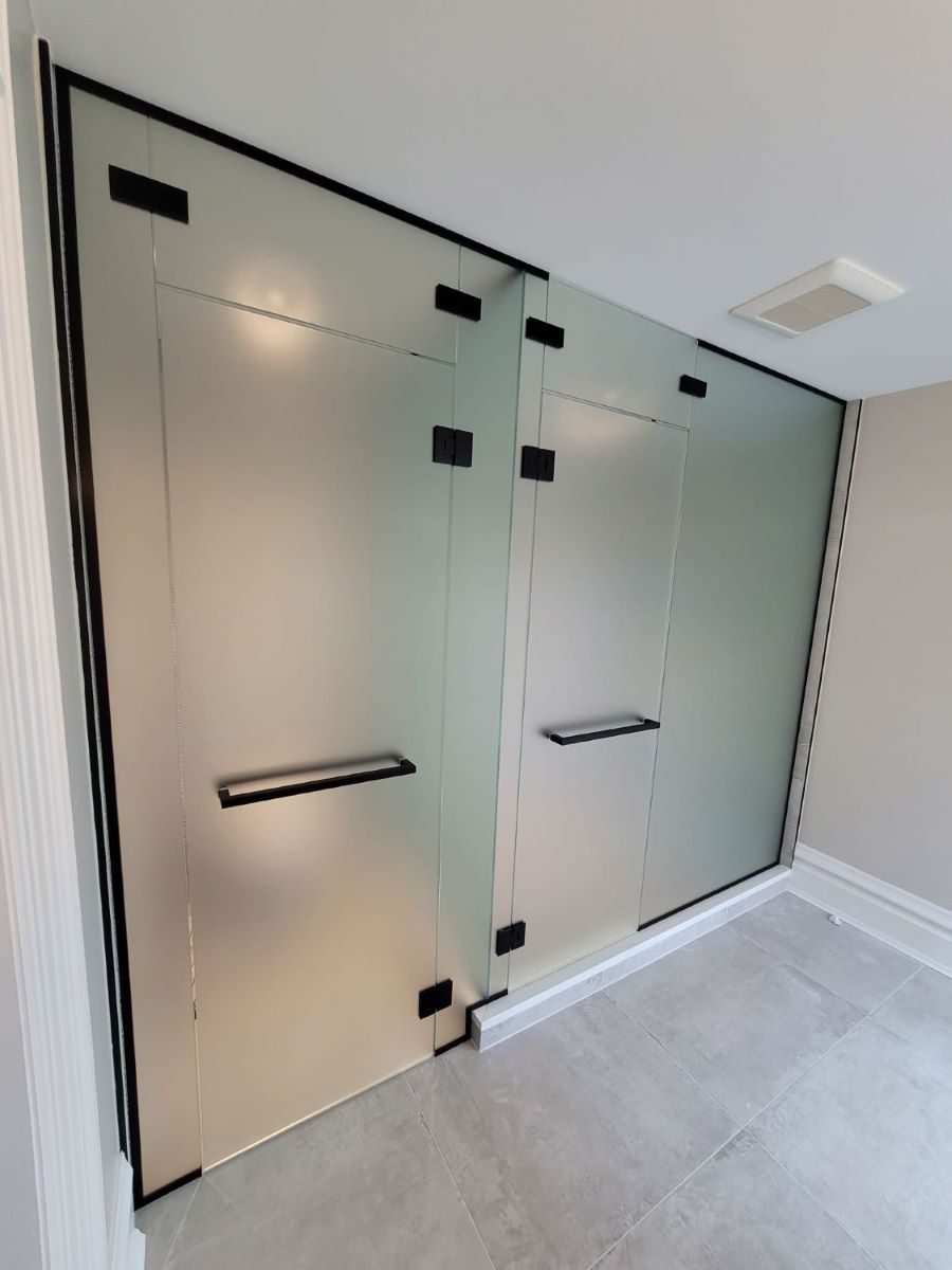 custom glass washroom and shower door in frosted glass with 2 transoms over the doors and matte black double towel bar handles