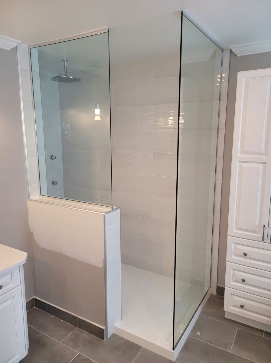 open concept shower with 2 glass panels one installed on a knee wall and chrome hardware 